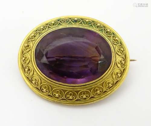 A Victorian brooch set with facet cut large large amethyst within a cannetille yellow metal mount.