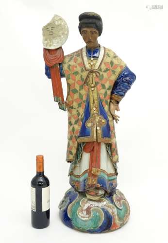 A tall Chinese ceramic figure wearing robes and holding a roundel in one hand having a sun to