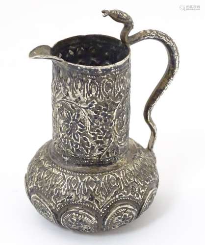 A small white metal jug with floral and foliate decoration and snake formed handle. Probably Indian.