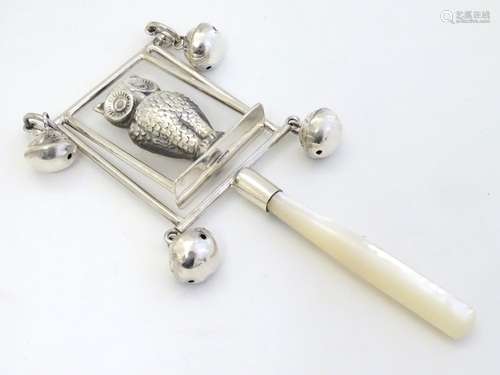 A white metal children's rattle with owl decoration, bells and mother of pearl teether.