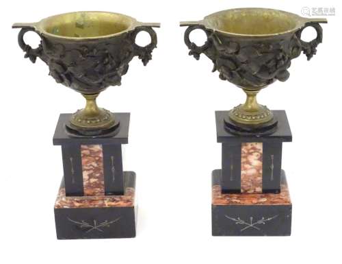 Garnitures : A pair of cast bronze pedestal cup urns on slate and marble bases.