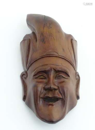 An Indonesian carved wooden wall hanging mask with hat. Bears old label verso.