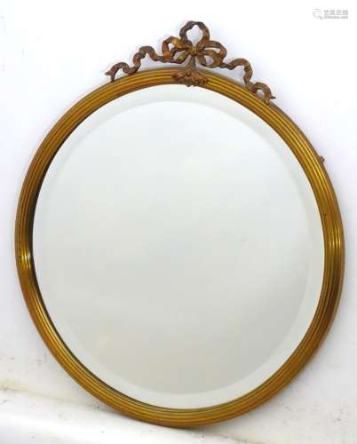 A late 20thC / early 21stC circular brass mirror with reeded edge and floral ribbon pediment.