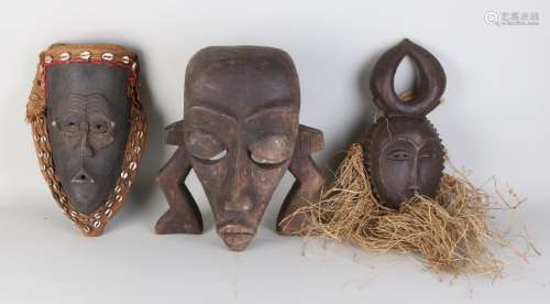 Three old woodcut African masks with shells and crop.