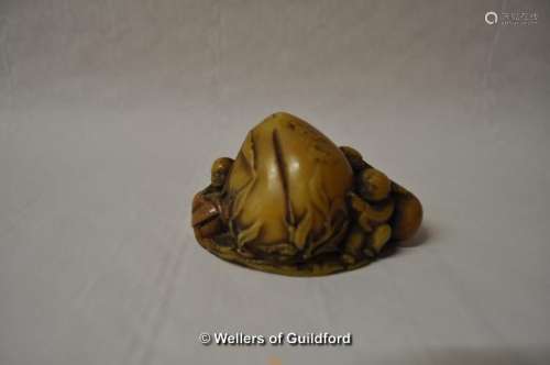 A Chinese yellow stone carving of children playing around a large fruit, 8cm long.