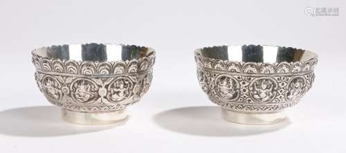 Pair of Oriental white metal bowls, with arch cast rims and bodies with depictions of deities, on