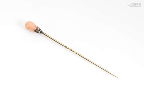 An early 20th Century diamond and coral stick pin, the pink pear shaped coral bead surmounted in a