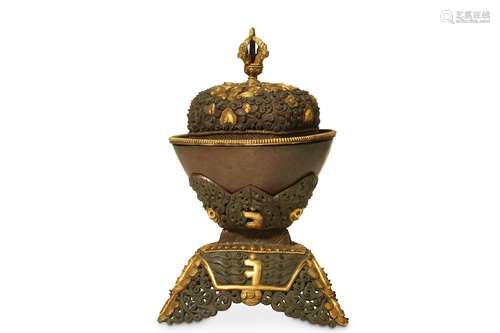 A TIBETAN GILT-BRASS REPOUSSE KAPALA WITH STAND AND COVER.  With a plain cup raised on a