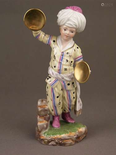 Musician from ''The Turkish Orchestra''- Hoechst, Germany, blue wheel mark with painter's<br />mark, bottom marked ''300 years German porcelain / Edition 2010 / 1/3'', cymbals player, porcelain, glazed, polychrome painted and gold-plated, yellow jacket and trousers with black pattern, on naturalistic pedestal, designed by Johann Peter Melchior (1747-1825), H.ca.18cm