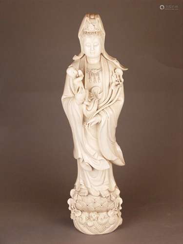 A Large Chinese Songzi Blanc de Chine Guanyin - Dehua, after 1900, exquisitely and<br />skilfully modelled, the elegant figure depicted standing on an open lotus flower, buffeted with beaded waves,wearing a layered robe draped over softly rounded shoulders and opening at the chest to reveal a beaded necklace , the head with a rather rounded face and long hair worked into a high top knot covered by a scarf and adorned with a tiara shaped as a portrait of the Buddha Amitabha, in her right arm she is cradling a little boy (the truth-seeking boy Sudhana/Chinese ' shancai'), naked except for a small bib, her left hand is holding a long-stemmed lotus flower, the eyes are downcast with lips gently indented to provide a benevolent expression, one lotus leaf (flower in her left hand) slightly chipped, the figure's back is impressed with the Dehua double gourd mark and the square artist's seal mark ''He Chaozong'',  H. approx. 70.5 cm, weight c.7.1kg