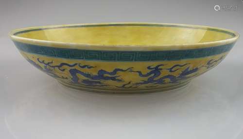 Dragon bowl - deep bowl, yellowish glaze as background,  underglaze blue five-clawed<br />dragon on the well, on vessel wall nine dynamically moving dragon in underglaze blue under green tinted meandering, base glazed white with underglaze blue mark in the double ring ''Da Ming Xuande Nian Zhi'', with Tianjin Jian Ding Export Seal, D.ca.25cm / H.ca.5,5cm