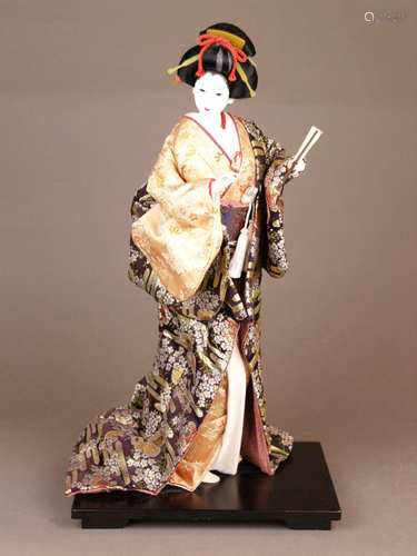 Nishi-Puppe - Japan, 20.Jh., stehende Geisha-Puppe mit anmutigem Gesichtsausdruck,<br />bekleidet mit reich dekoriertem wattiertem Seidenkimono, einen losen Fächer in der Hand haltend, auf schwarz lackiertem Holzsockel, H.(ohne Sockel):ca.42cm