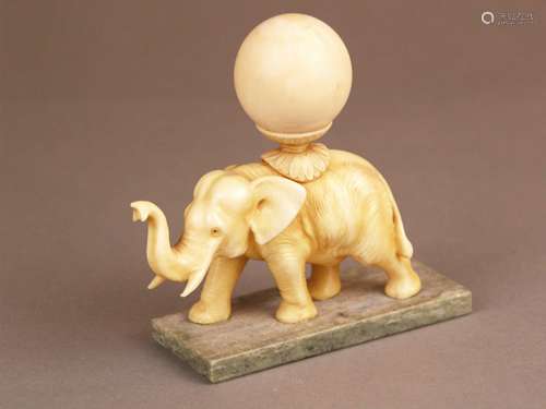 Ivory carving ''Elephant carrying a globe'' - India c.1920 / 30, full round depiction of a<br />striding elephant with a large lotus stand supported globe on its back, mounted on rectangular light green onyx plate, one corner slightly uneven, H.c.11cm