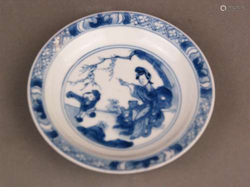 Small blue and white dish with figures in a landscape - China, Qing Dynasty, underglaze<br />blue decor featuring a lady sitting under a tree, in front of her a grimacing boy, the rim edged in .and lotusleafs, treasures to the outside, underneath four-character mark ''Cheng hua nian zhi ''(Chengua reign 1465-1487) but later Kangxi (1662-1722), some small glaze irregularities to the stand ring