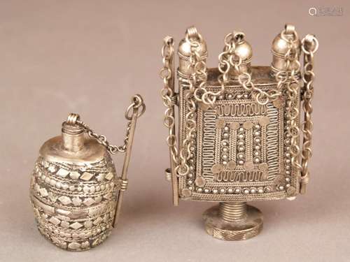 Two flasks- Yemen, metal alloys with silver content, 1x rectangular flask on a round base,<br />with elaborate silver overlays, above three elevations, of which two lateral with openings, plug-in closure, two make-up sticks on chain, H.ca.9,5cm, 1x smaller flask in barrel form, plug-in closure, make-up stick on chain, h.ca.6cm, both with signs of age and use, weight together about 14g