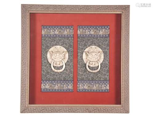 Pair of door knockers in object box - China / Tibet, round shape, in the center guardian<br />lion heads, movable rings, cast metal, four mounting holes, on red background and black brocade stripes with floral decoration as well as ribbons with processions and ruyi heads, framed under glass, frame with nuppen, D.(door knockers):ca.15cm, slight signs of age, frame ca.84x84cm