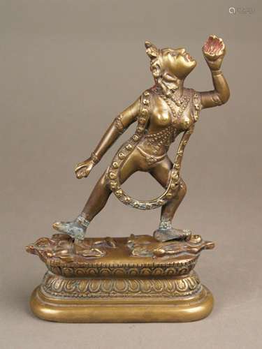 Bronze figure Dakini Vajrayogini - Sinotibetan, 20th century, gilt and paint, standing in<br />alidhasana on Vedic deities on a Lotos base, holding attributes, bejewelled and with a long skull chain, two-pieces: figure and a oval padmasana base, total height c.25 cm, base plate underneath with engraved double vajra, partly copper efflorescence to the figure