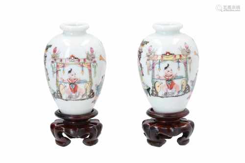 Two polychrome porcelain vases on wooden bases, decorated with little boys making music and a