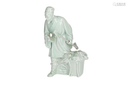 A celadon glazed Yixing sculpture, depicting a man holding a book, a bag of harvest and a spade.