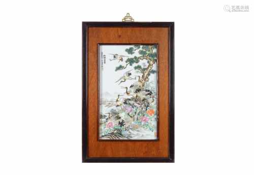 A polychrome porcelain plaque in wooden frame, depicting cranes, flowers and characters. Made in