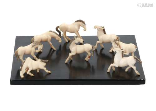 A set of eight carved ivory horses on wooden base. 