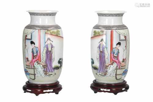 A pair of polychrome porcelain vases on wooden base, decorated with figures in a house and