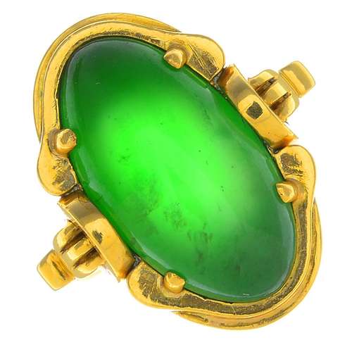 A jade ring. The oval jadeite cabochon, with grooved scroll surround and geometric shoulders.