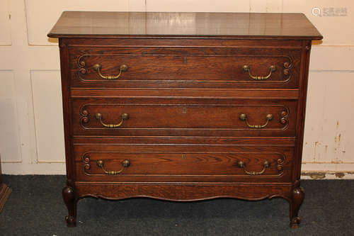 An oak chest of three drawers with carved panel fronts and brass drop handles, on cabriole front