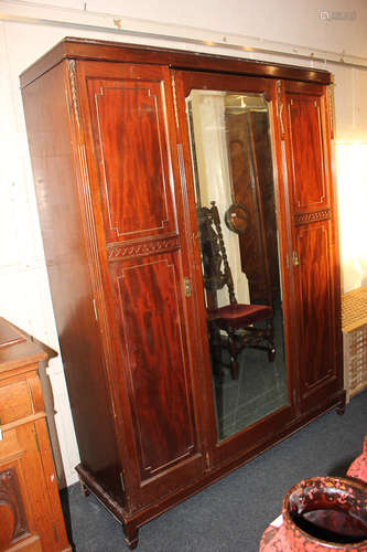 A mahogany triple door wardrobe, with central full length mirror door, flanked by panelled doors,