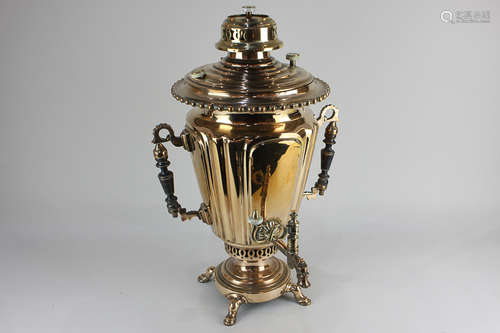 A brass samovar with two decorative turned wood handles and circular base, raised on four feet,