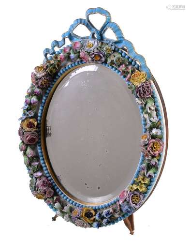 An English porcelain flower encrusted oval looking glass frame with wood easel stand, surmounted