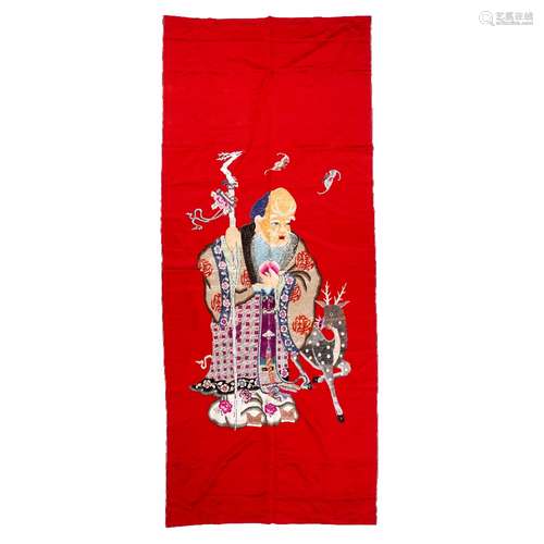 Red ground fabric panel Chinese depicting a standing Luohan with a staff in one hand and a deer by