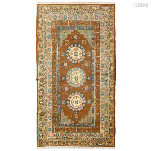 KHOTAN CARPET EAST TURKESTAN, LATE 19TH/EARLY 20TH CENTURY the brown field with three cream and blue