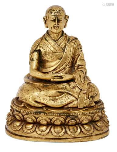 A Tibetan gilt bronze figure of a lama, 17th century, with hands clasped in his lap, wearing a