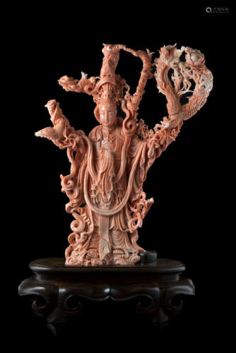 A large coral branch carved with Guanyin wearing ornate robes and jewelry, carrying the elixir