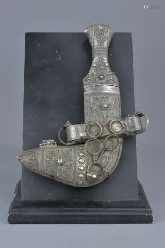 A Yemenis silver-coloured metal dagger in a case on later display stand. 29cm length