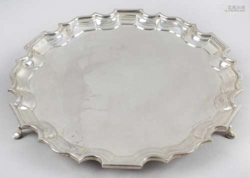 A 1920's small silver salver, of circular form with scalloped rim, and raised upon three pad feet.