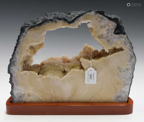 A quartz crystal geode cross-section of creamy yellow tone, 28cm x 35cm, mounted on a wooden stand.