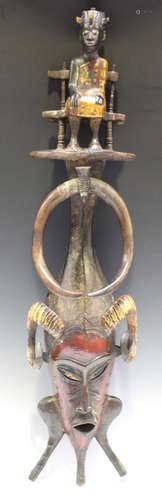 A Senufo carved and painted wooden mask, Ivory Coast, the surmount modelled as a seated figure above