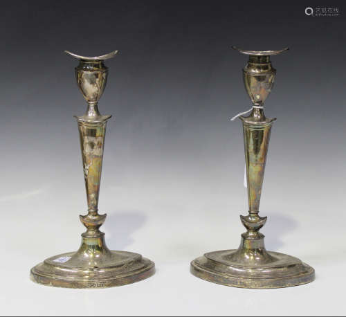 A pair of Edwardian silver candlesticks, each urn shaped sconce above a tapering stem and oval foot,