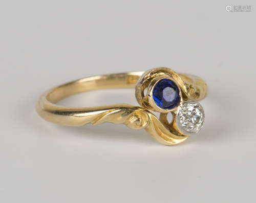 A gold, diamond and sapphire two stone cross-over ring, collet set with a circular cut diamond and a