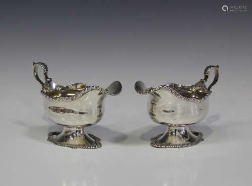A pair of Edwardian silver sauce boats, each with gadrooned rim and scroll handle, raised on a