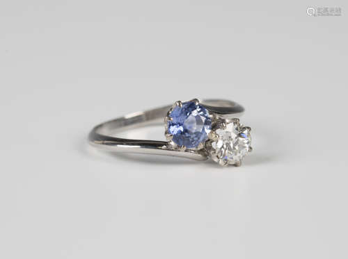 A diamond and Ceylon sapphire two stone cross-over ring, claw set with a circular cut diamond and