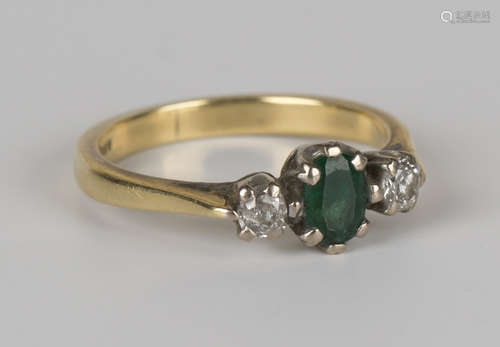 An 18ct gold, emerald and diamond set three stone ring, claw set with the oval cut emerald between