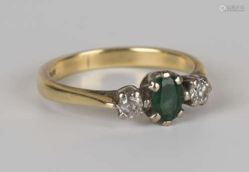 An 18ct gold, emerald and diamond set three stone ring, claw set with the oval cut emerald between
