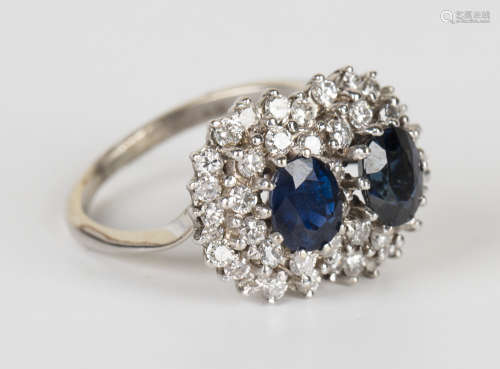 An 18ct white gold, sapphire and diamond ring in a twin cluster cross-over design, claw set with two