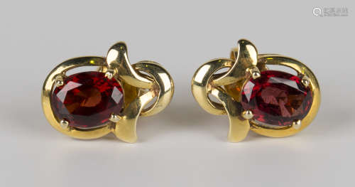 A pair of gold and garnet earrings, each claw set with an oval cut garnet within a scroll