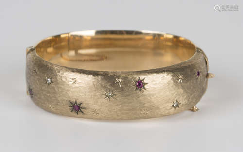 A 9ct gold, diamond and ruby set oval hinged bangle, decorated with star motifs against an engine