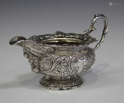 A late George III silver cream jug, chased with scrolling foliage framing two vacant cartouches,