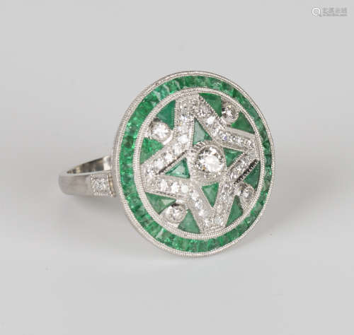 A platinum, emerald and diamond cluster ring, collet set with the principal circular cut diamond